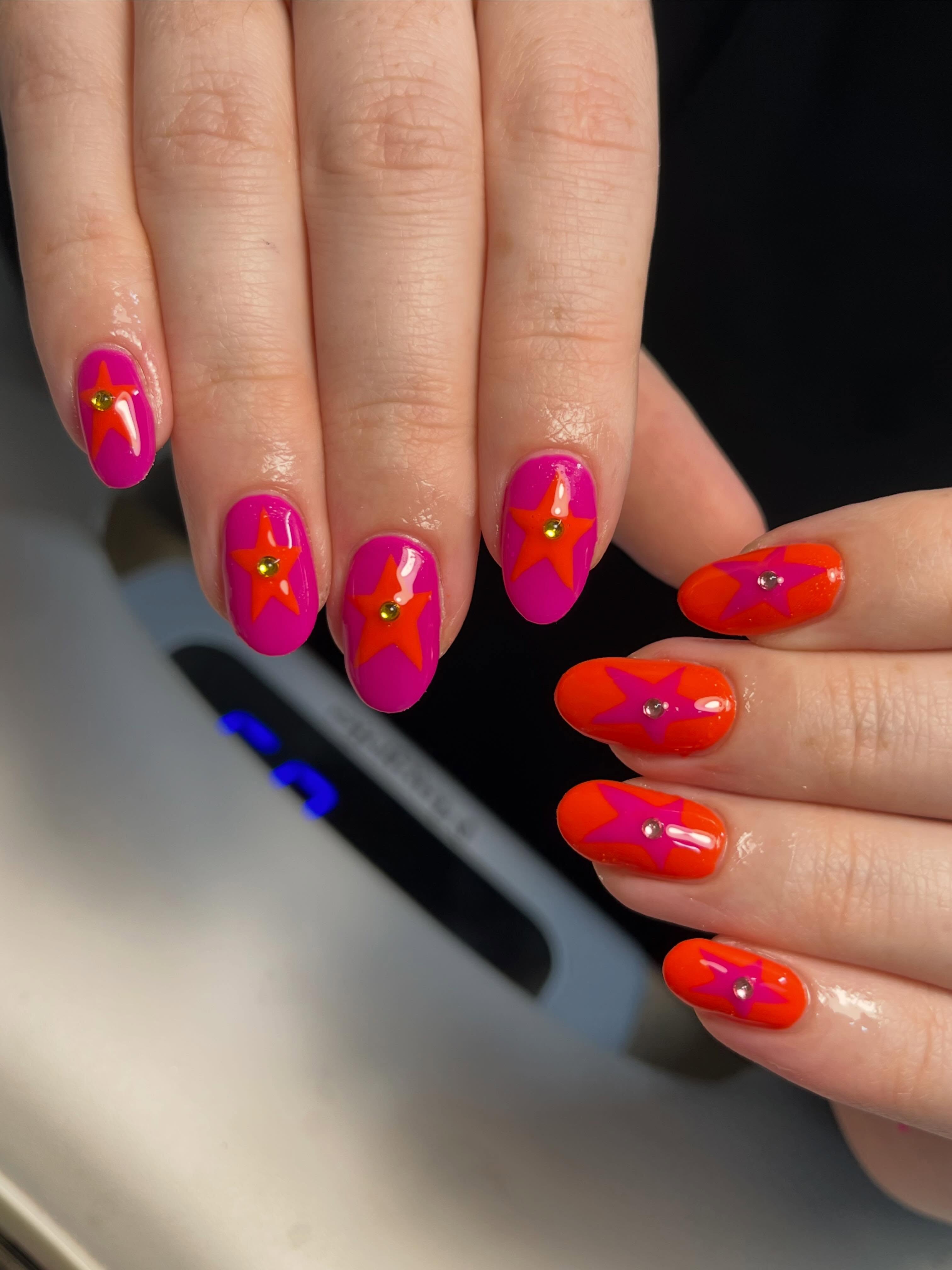 Bright pink and orange star nail art with rhinestone accents on short oval nails, a bold, playful summer design