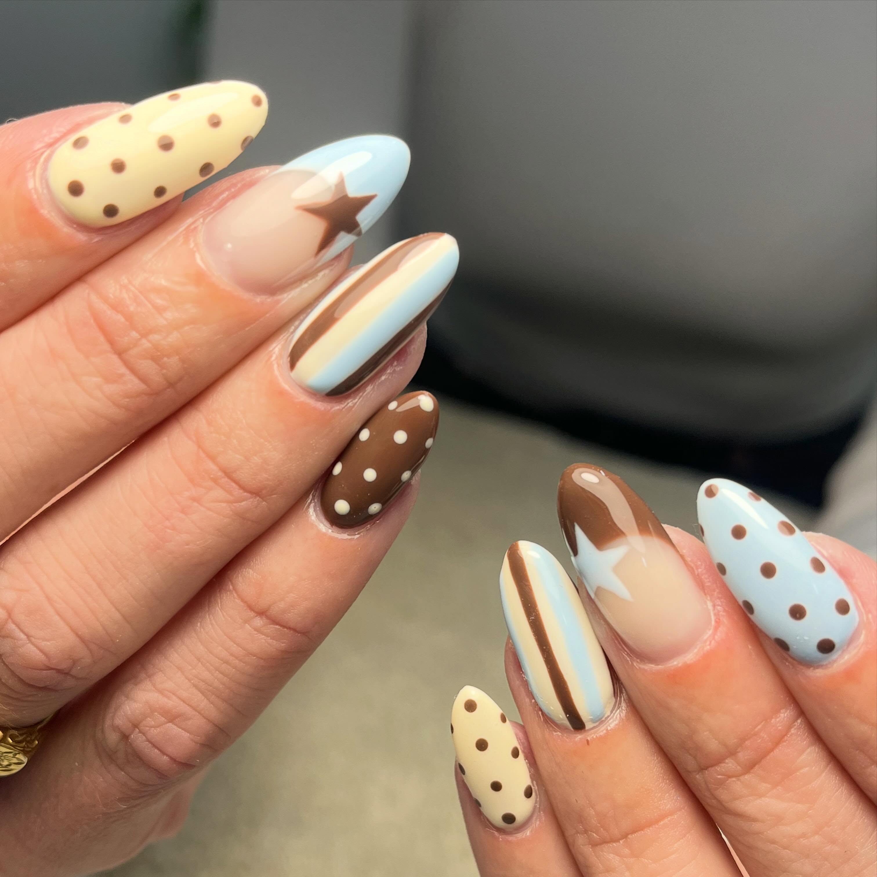 Retro-inspired nail art with pastel blue, cream and brown stripes, polka dots and star accents on almond-shaped nails