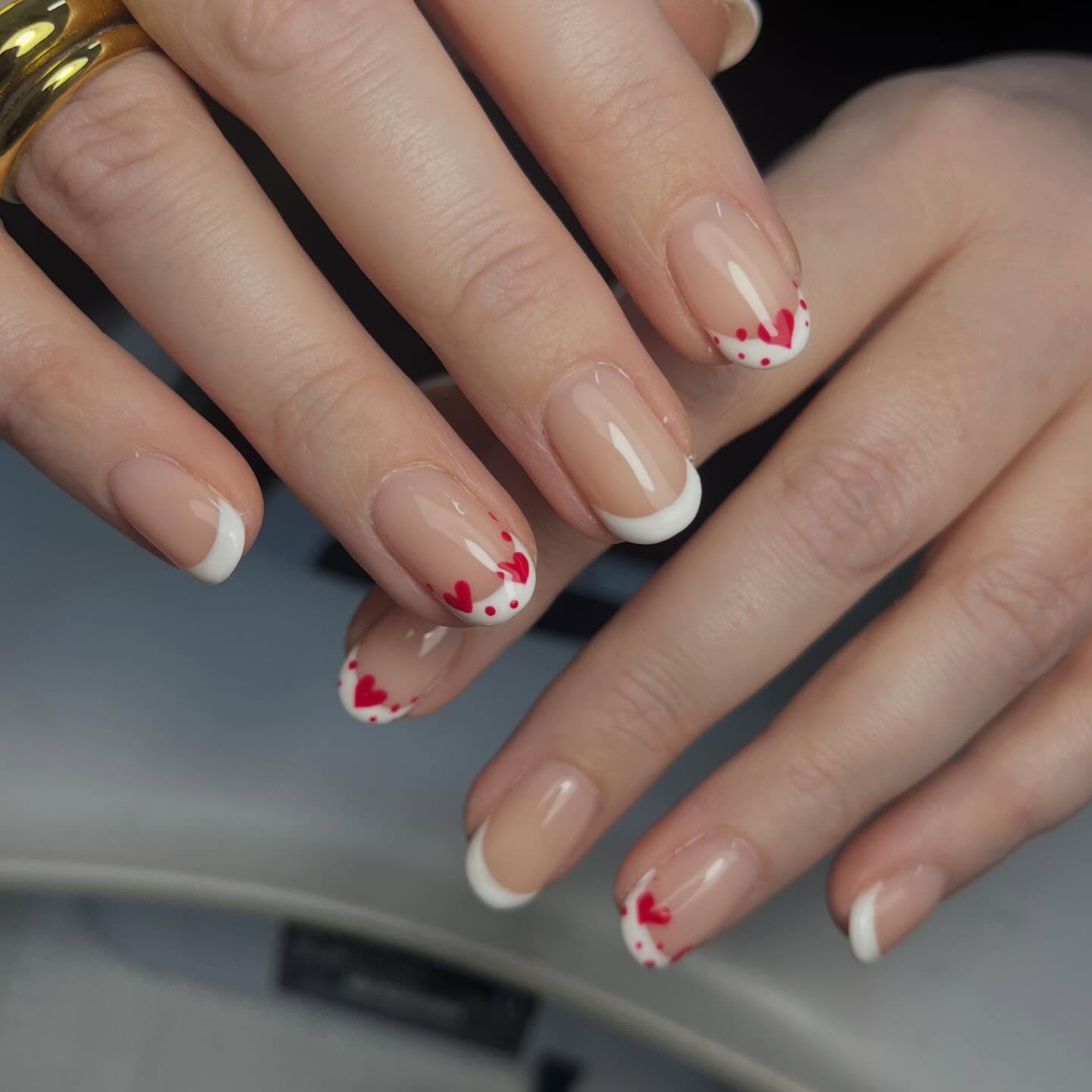 Classic French manicure with delicate red heart details and romantic Valentine's-inspired nail art on short natural nails